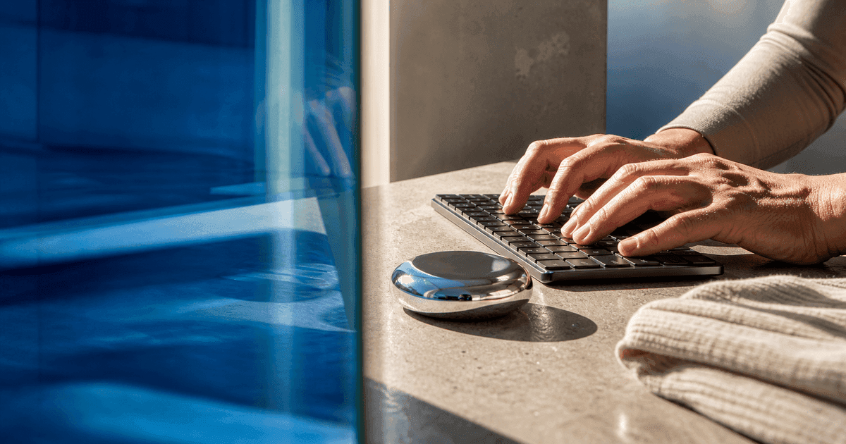 Adult hands type beside cobalt glass that sharpens the work area and refracts the edges