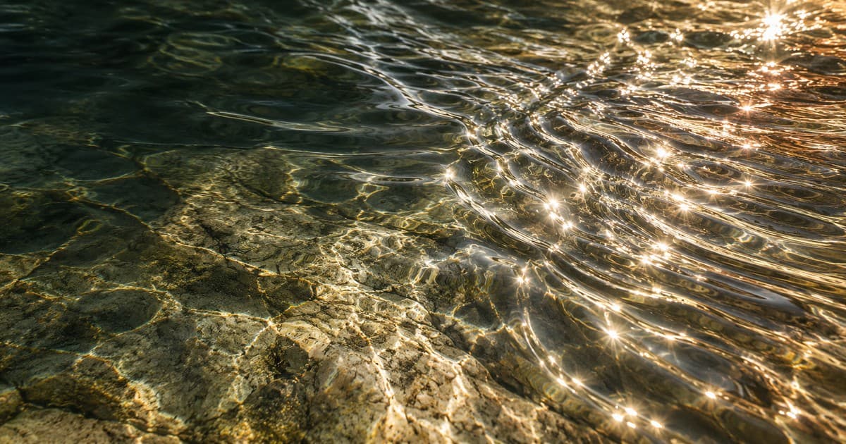 Two ripple patterns meeting in shallow mineral water, with silver light and a warm copper reflection.