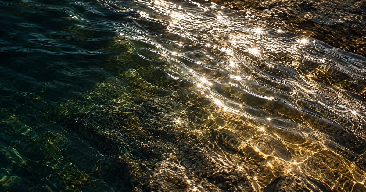 Silver and copper sunlight breaking across ripples over dark submerged stone.