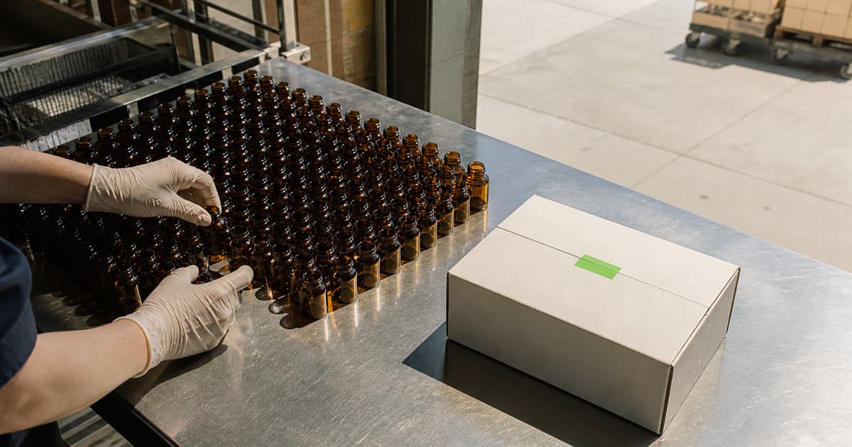 Gloved hands arranging amber pharmacy vials beside one complete unlabeled care package