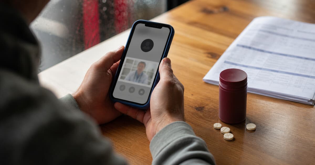 Hands holding a phone during an online visit beside a burgundy Enclomiphene jar, flex-dose tablets, and lab paperwork