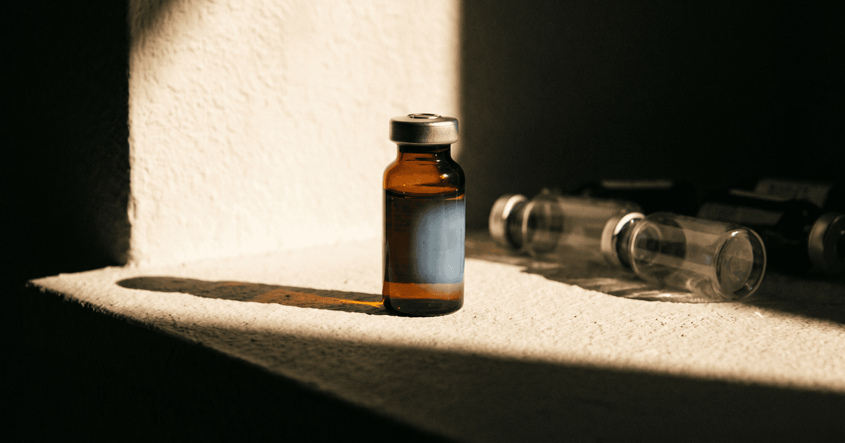 One sealed capped amber vial lit in hard daylight beside unlabeled anonymous vials receding into shadow.