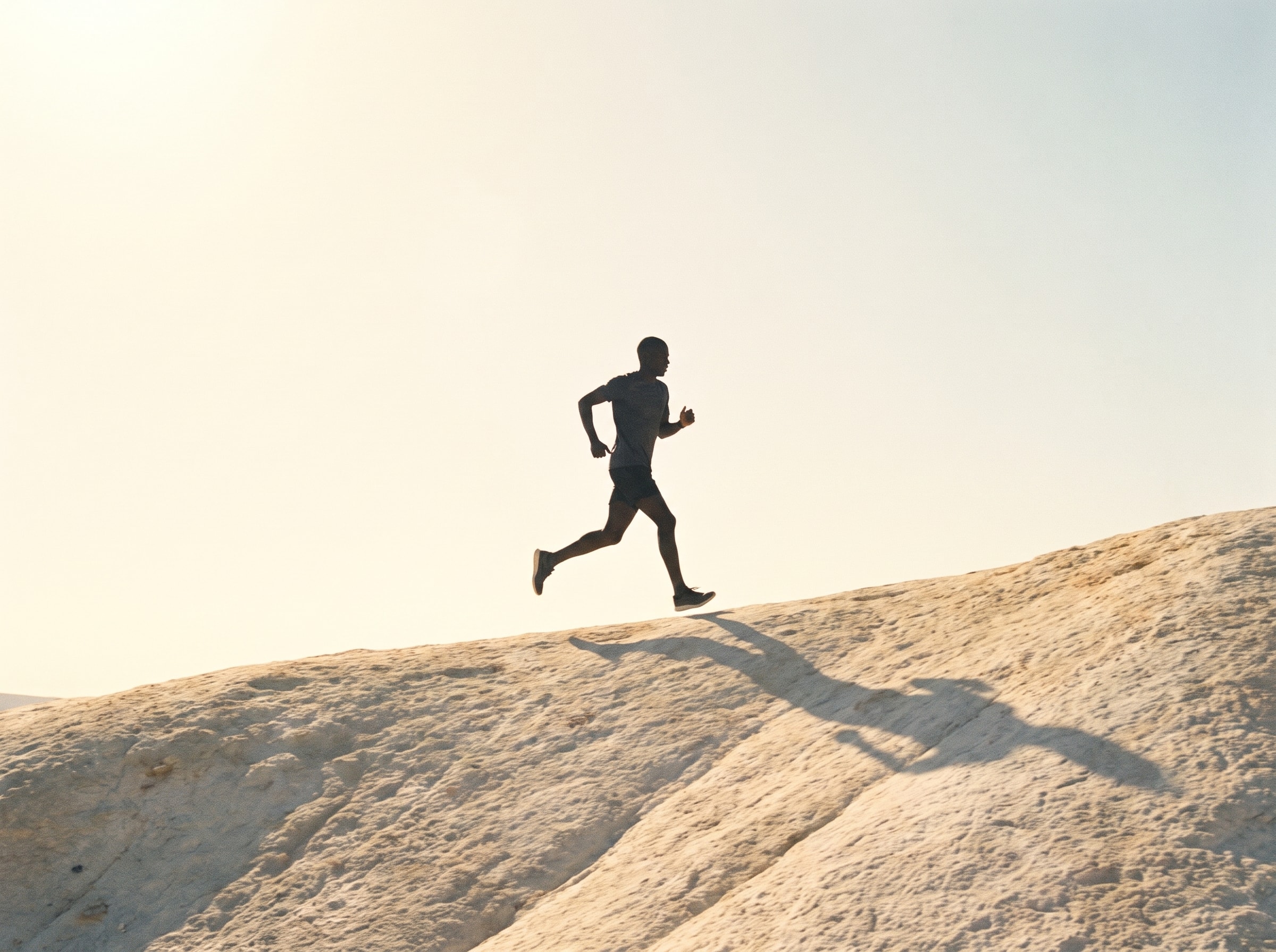 A runner moves across a sunlit mineral ridge.