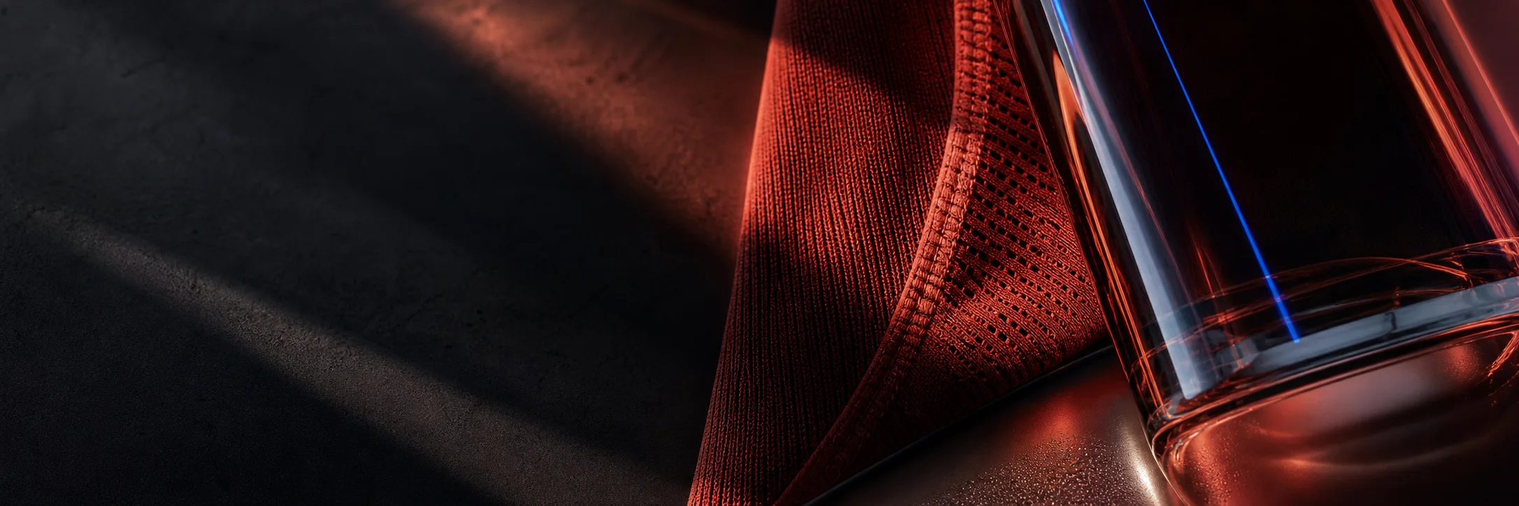 Red knit fabric and a dark glass catching warm light on slate stone.