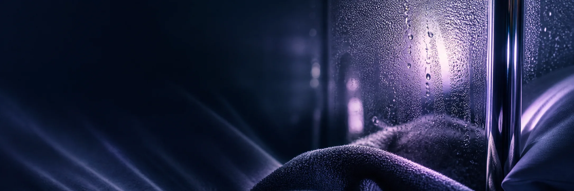 Condensation on dark glass beside a soft pillow in low purple night light.