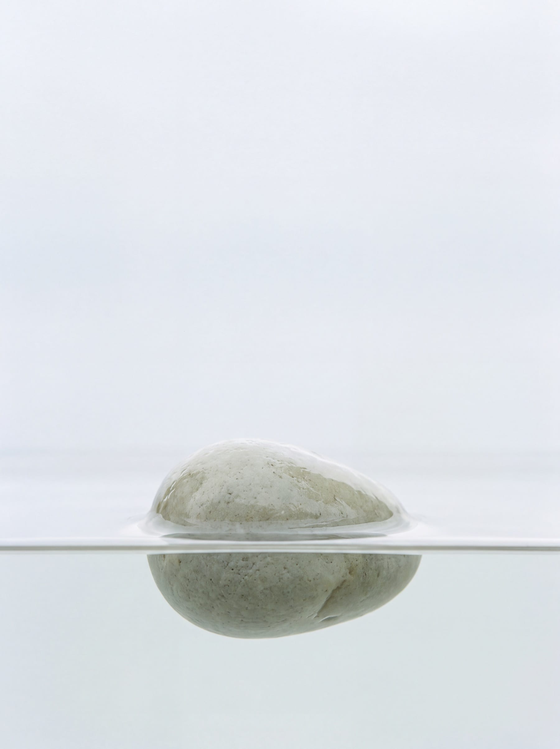 A pale stone resting at the surface of still water, with one clean waterline across the frame.