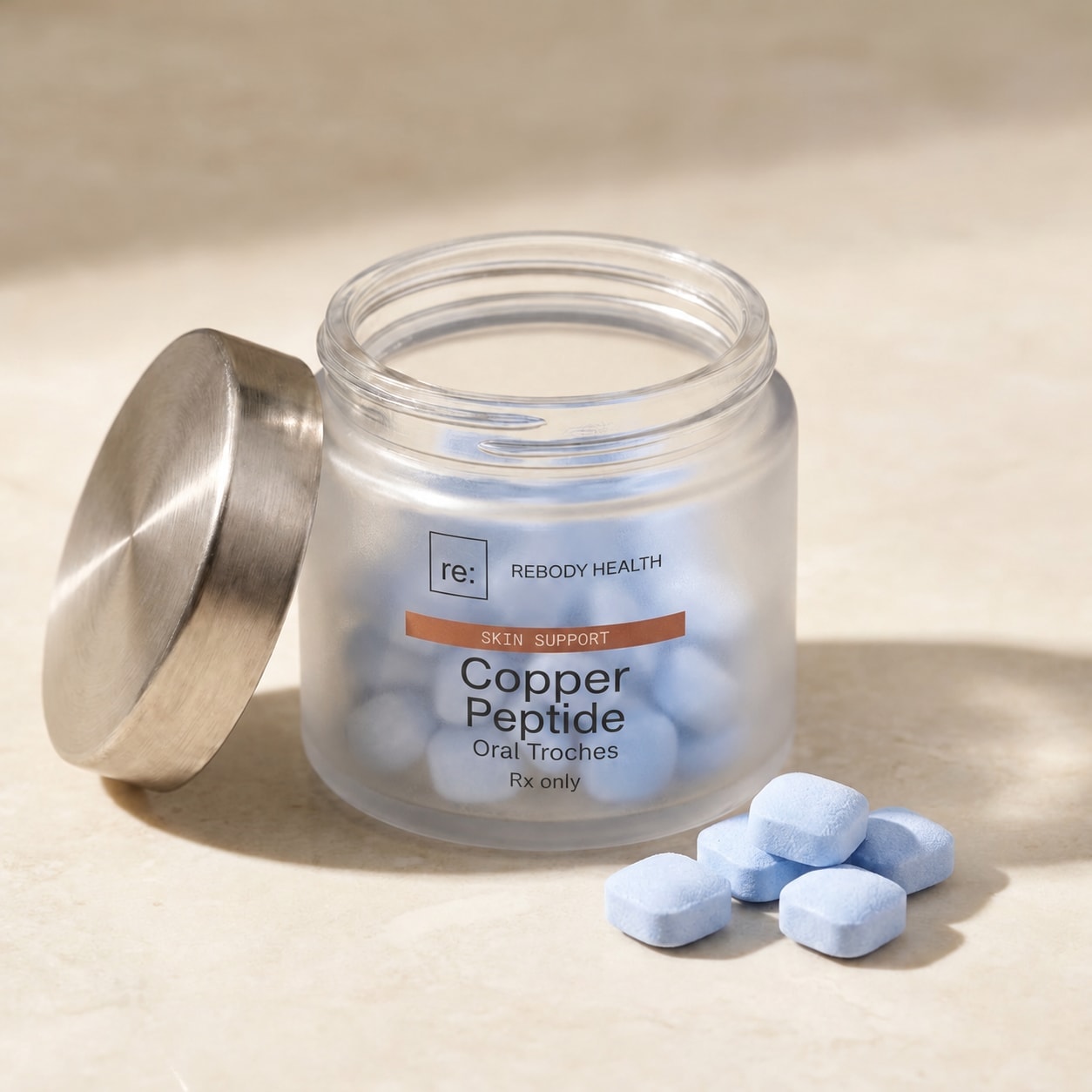 Pale blue Copper Peptide troches on stone beside the open frosted jar and its silver lid.