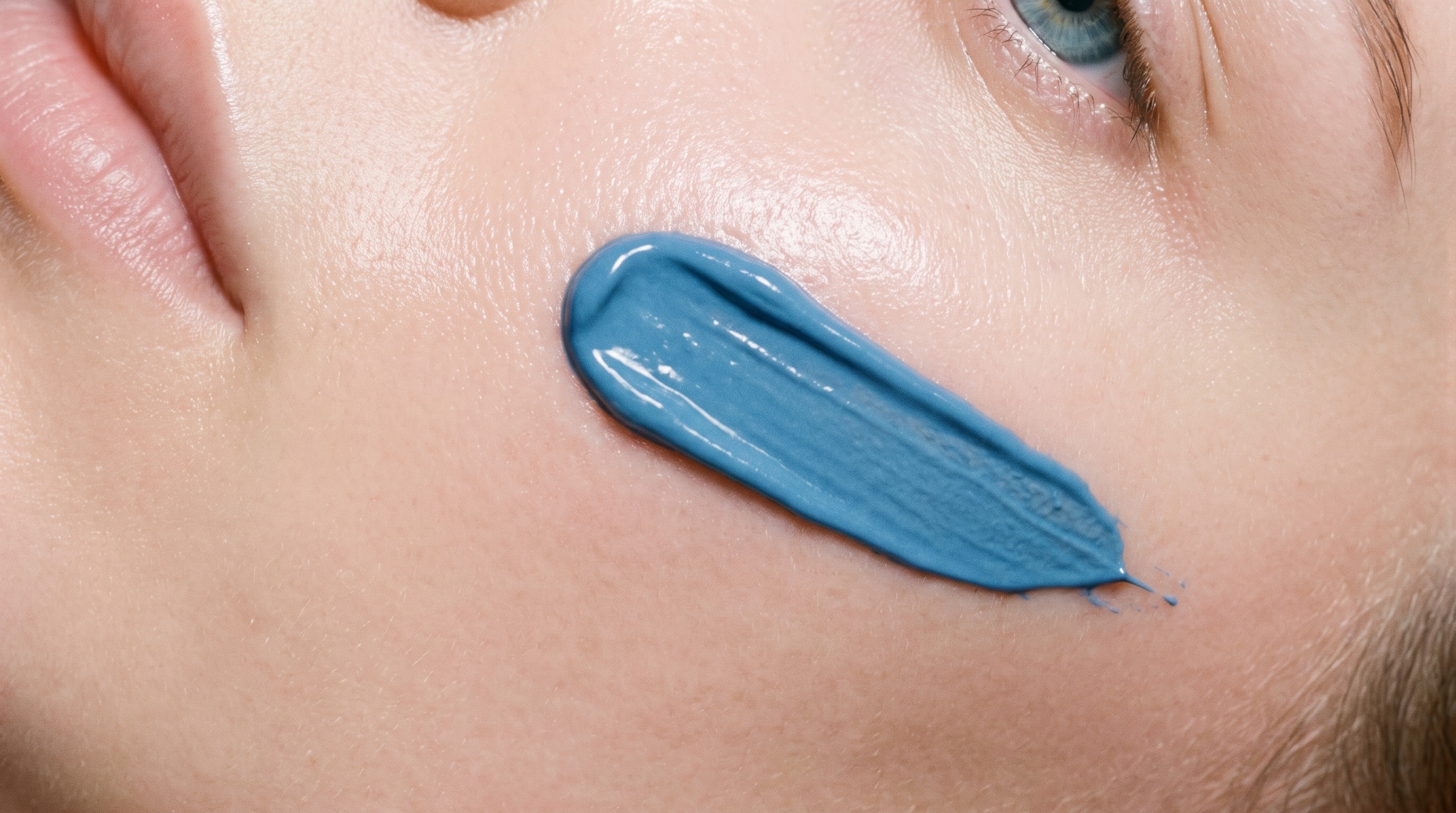 A close crop of facial skin with a mineral-blue streak of GHK-Cu cream across the cheek.