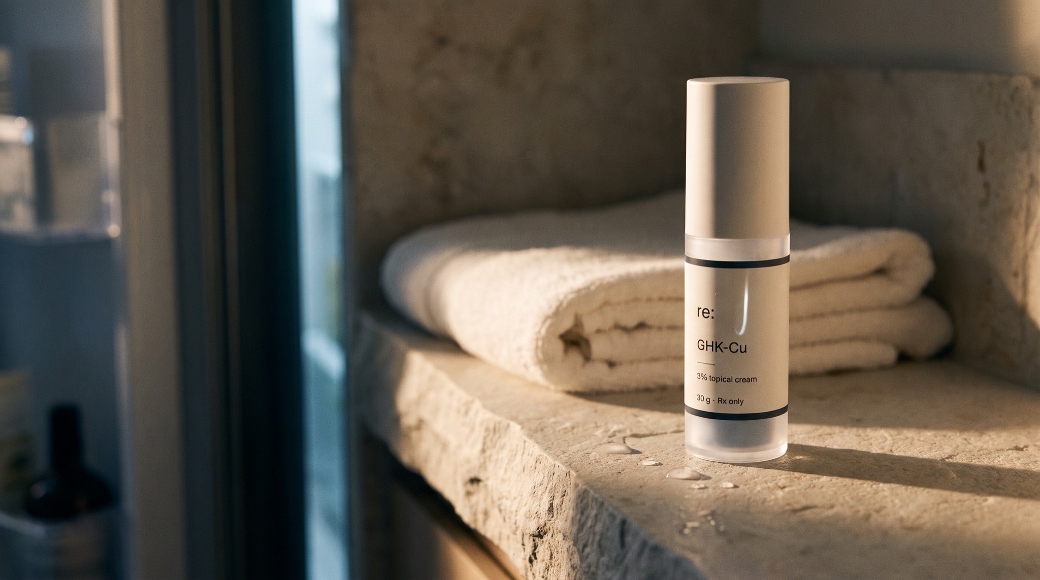The GHK-Cu cream pump on a cool stone shelf beside a folded towel in low evening light.