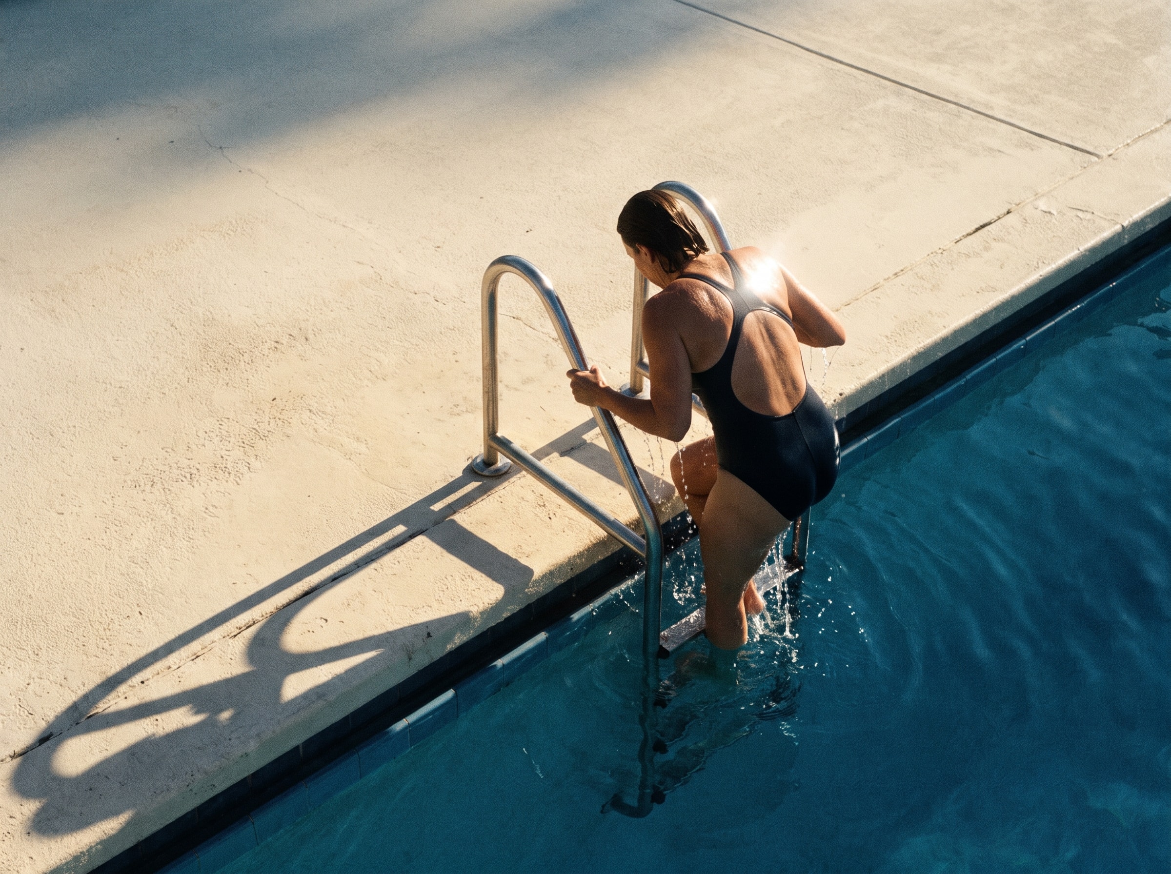 A swimmer pulls herself out of an outdoor lap pool in late afternoon sun.