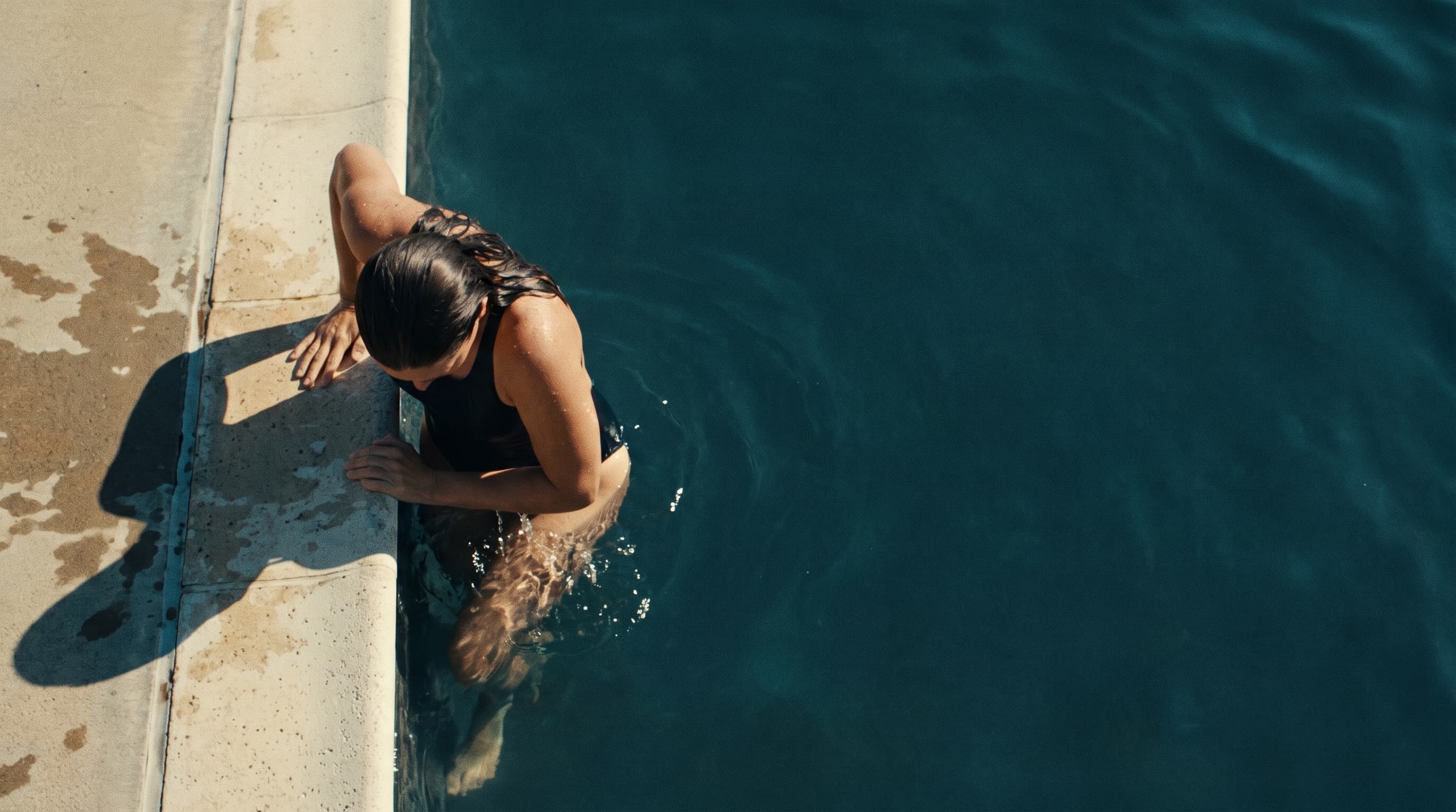 Swimmer resting at the edge of deep blue water, seen from directly overhead