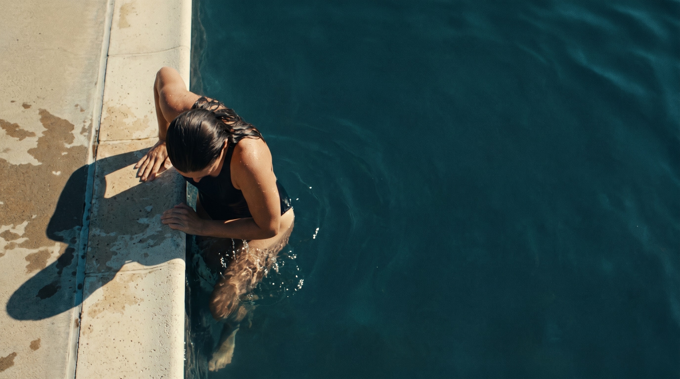 A swimmer rests at the edge of a sunlit pool after a morning session.