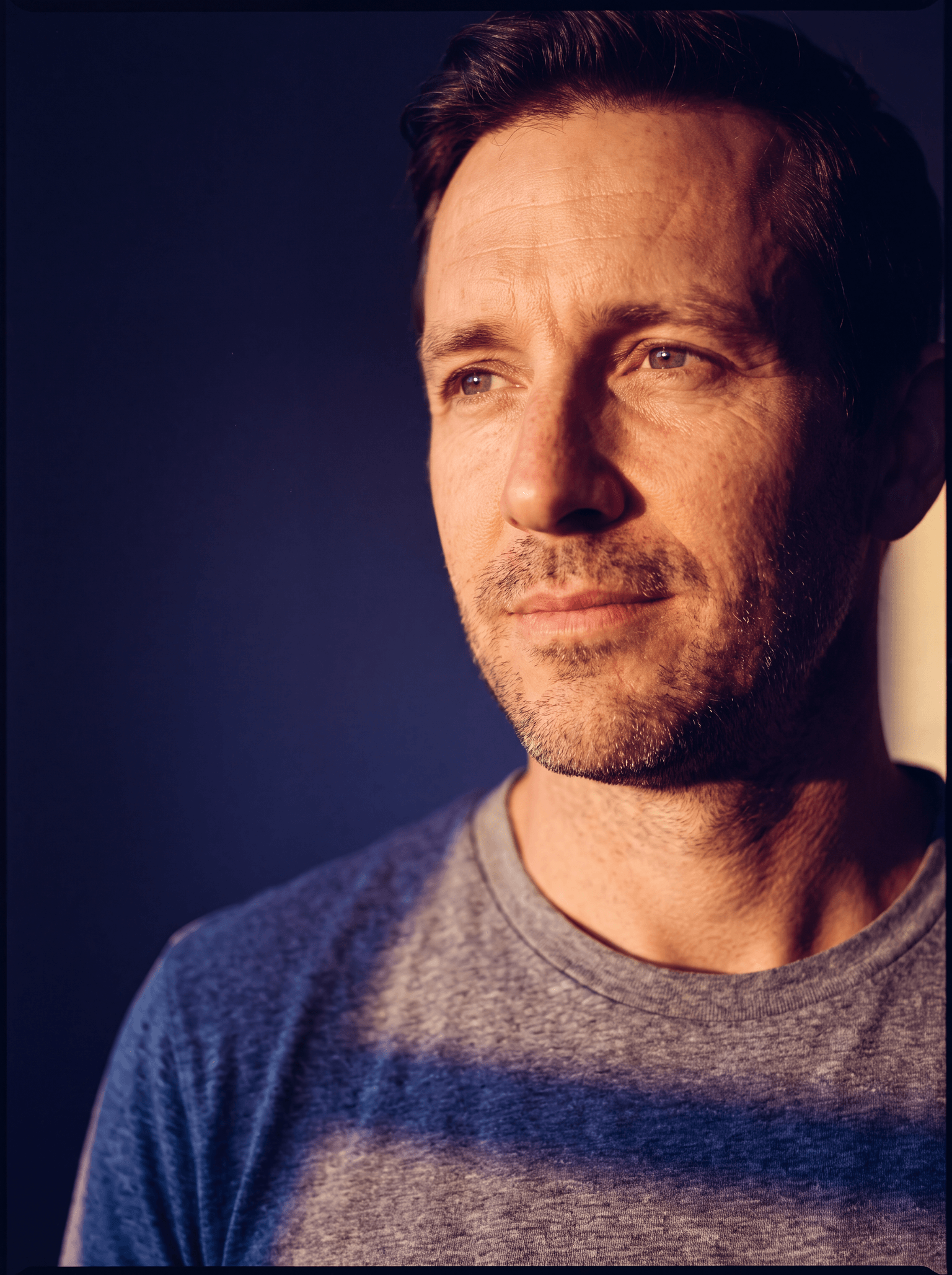 Man in his forties sitting up rested at the edge of the bed in cool violet dawn light, calm and renewed.