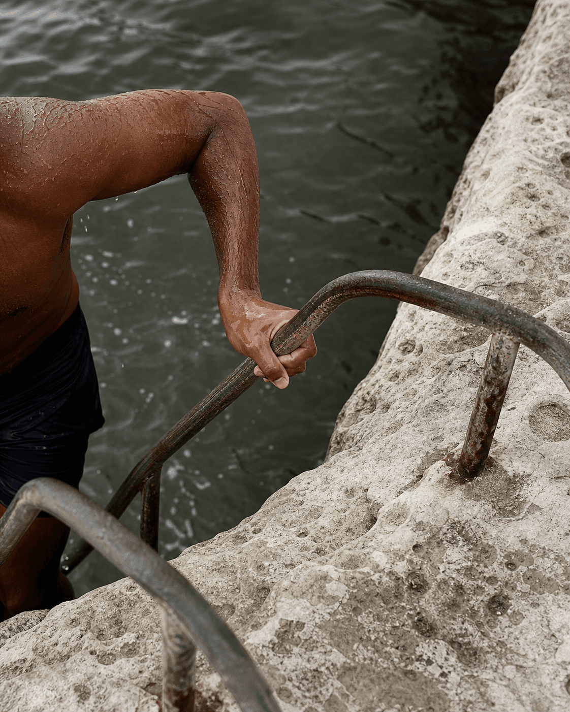 Wet swimmer gripping a weathered sea ladder beside limestone