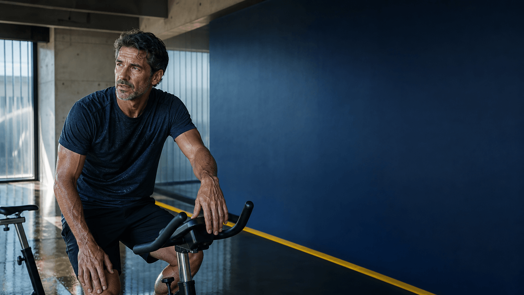 Man pausing over a stationary bicycle after a demanding interval session.