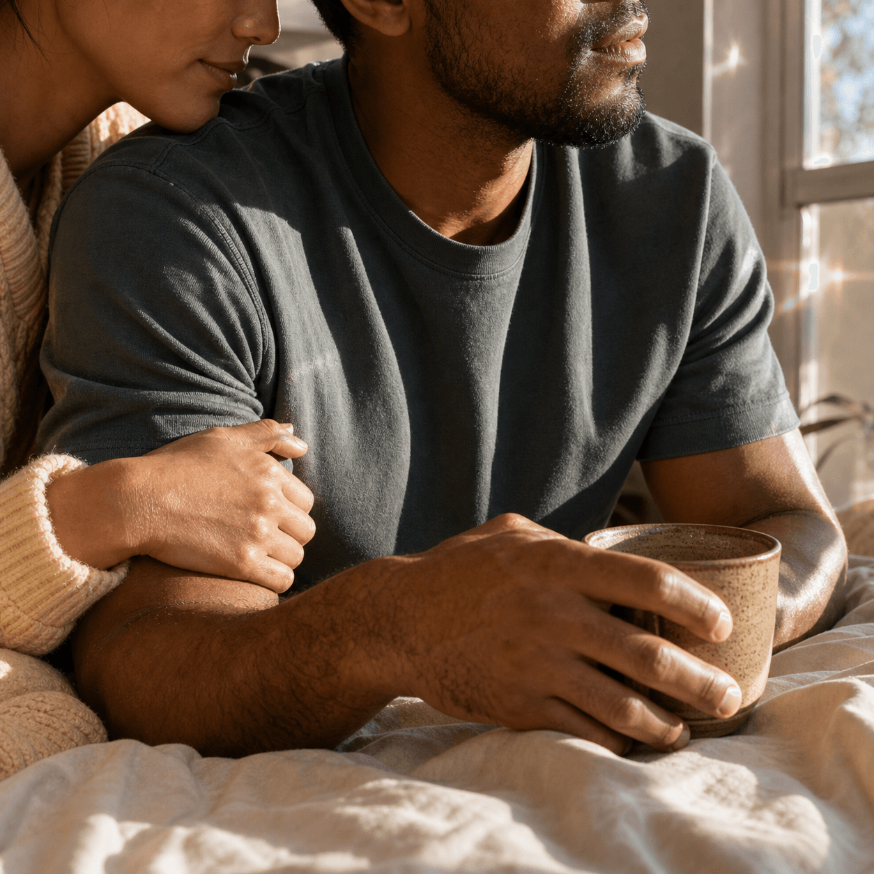 Couple sitting close in warm window light with hands resting together.