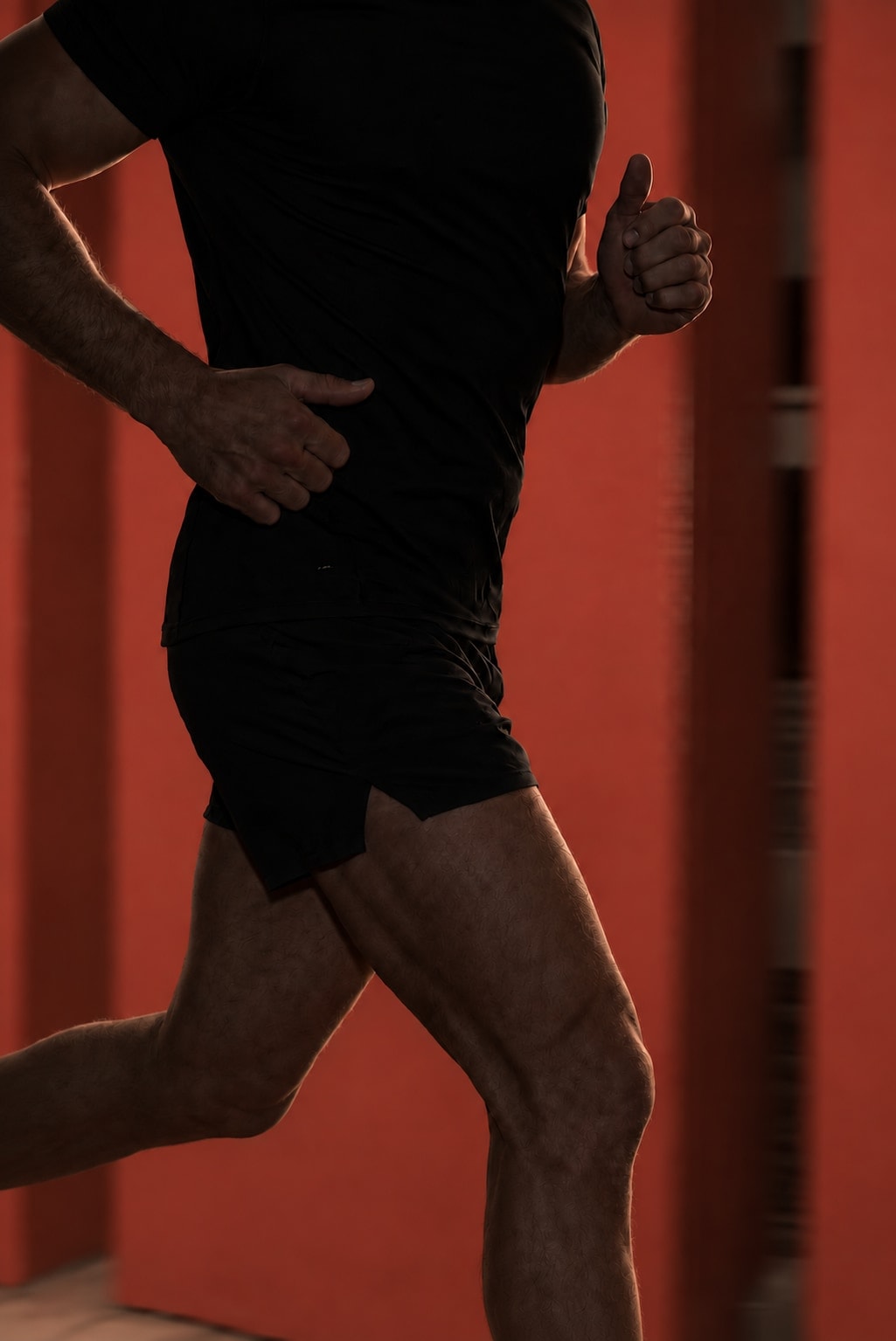 Cropped runner in deep shadow against an oxide-red background, with light tracing his arms and legs.