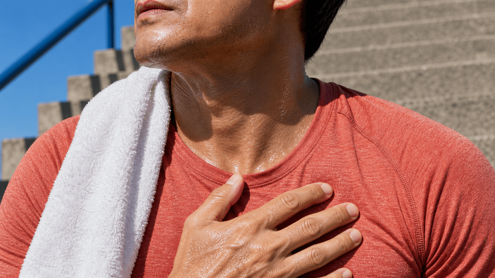 Adult after outdoor exertion with a towel over one shoulder and a hand resting on the chest.