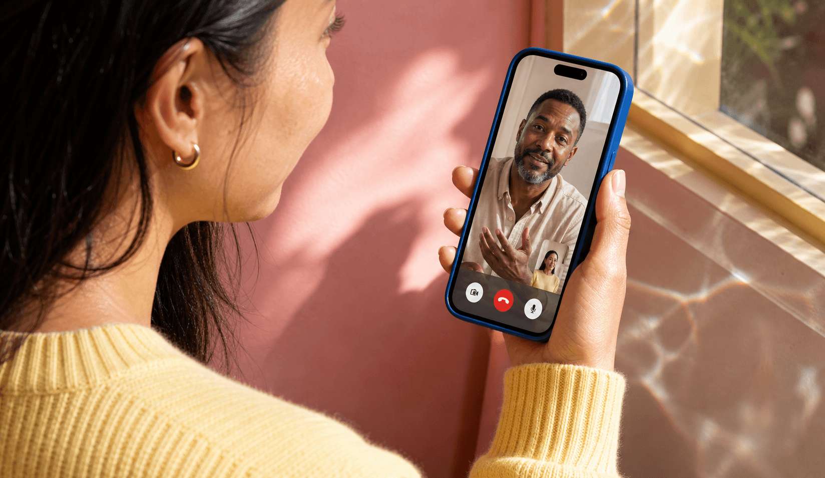 Woman in a yellow sweater holding a smartphone for a video visit with a provider.