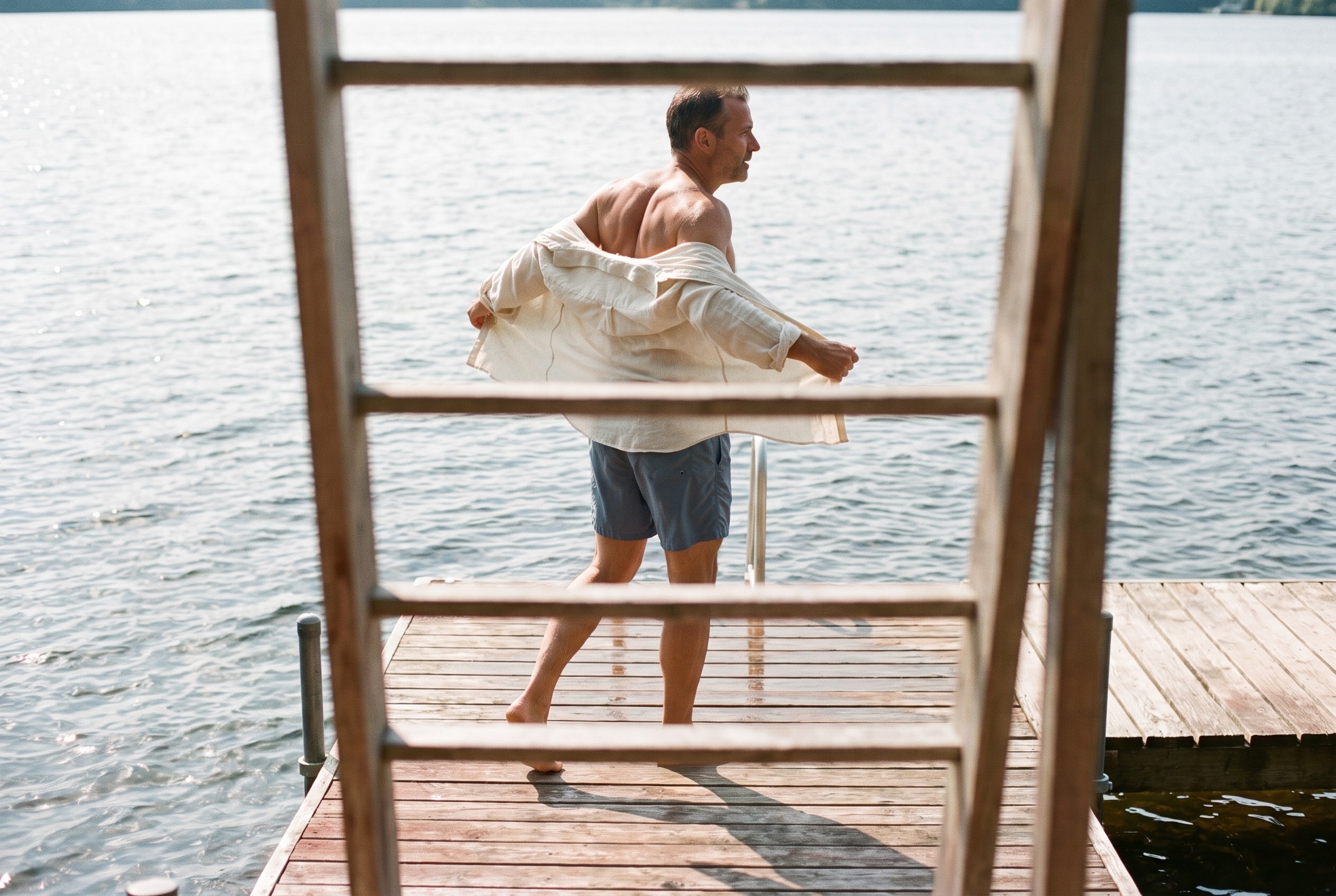 A swimmer shaking out a towel on a wooden jetty above open water.