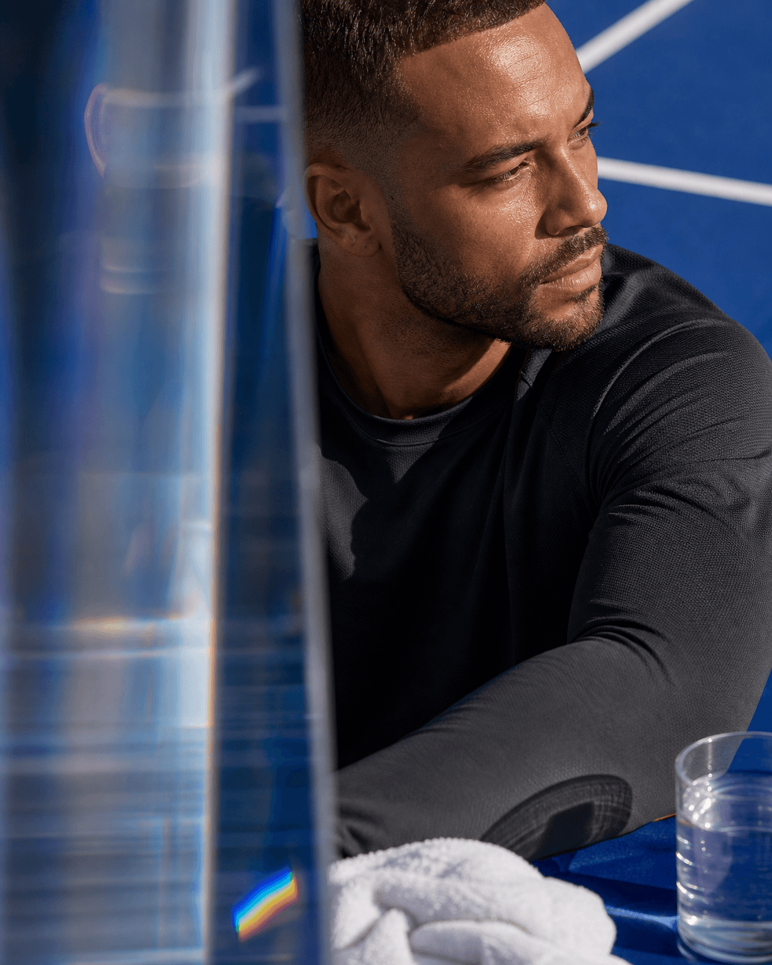 Man pausing after training as refracted light crosses a cobalt court.