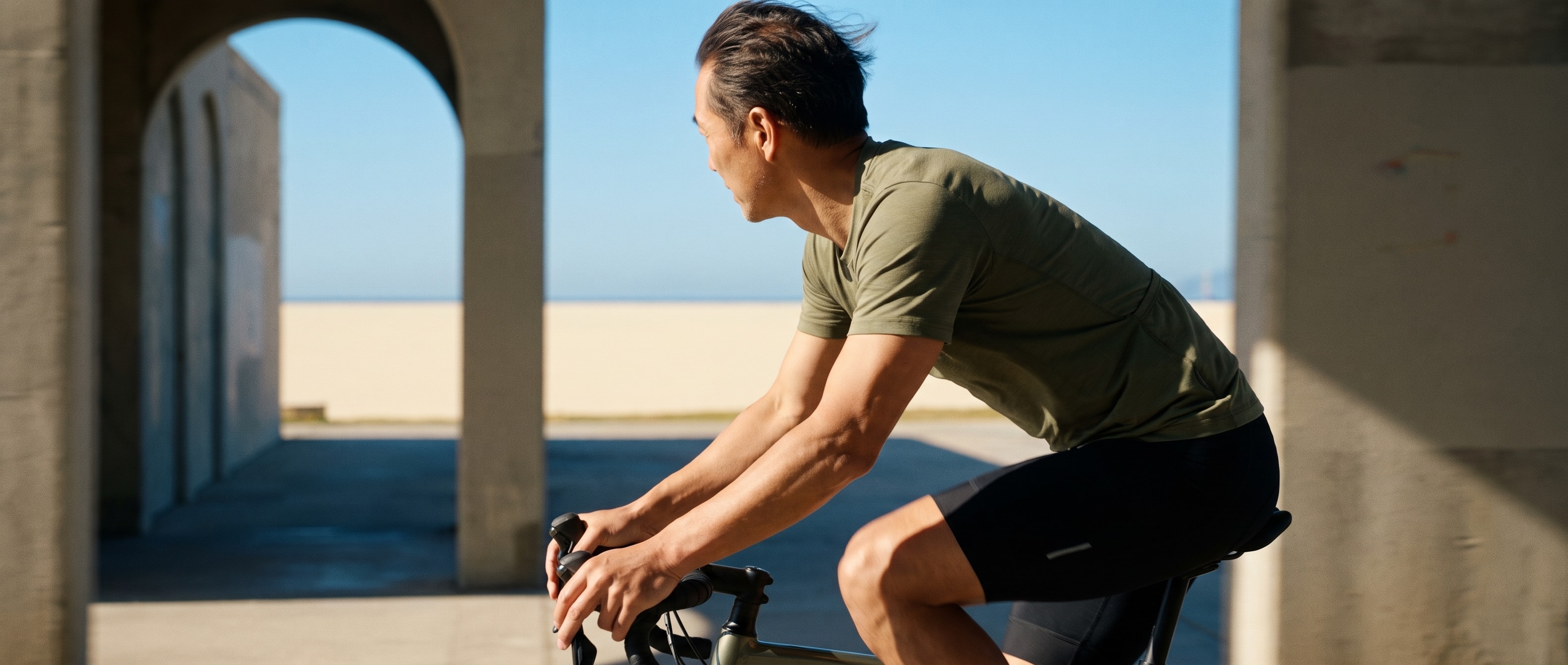 A cyclist rides through a sunlit coastal colonnade.